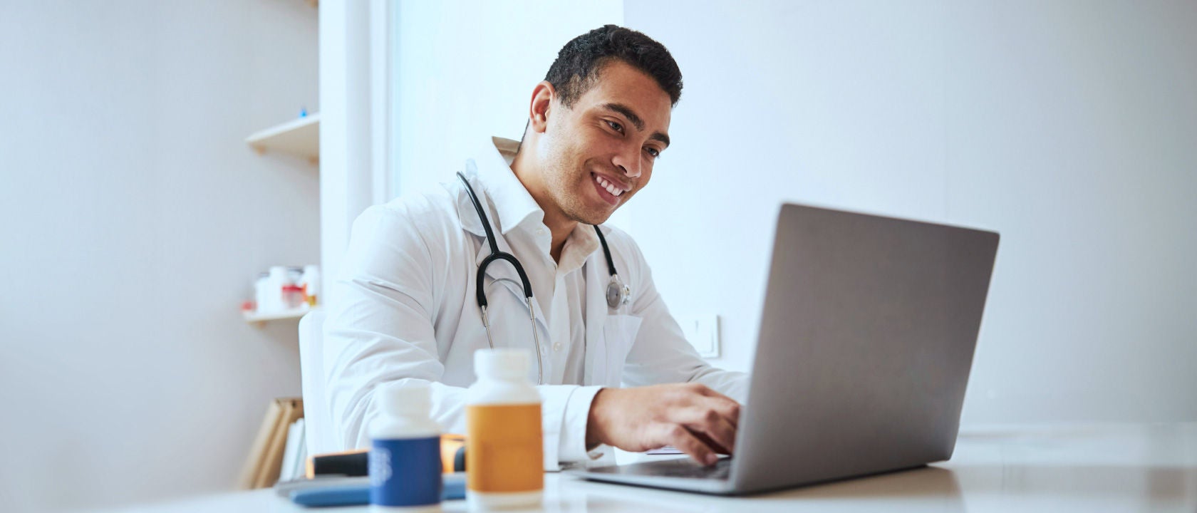 Photo of male doctor using laptop in a white office