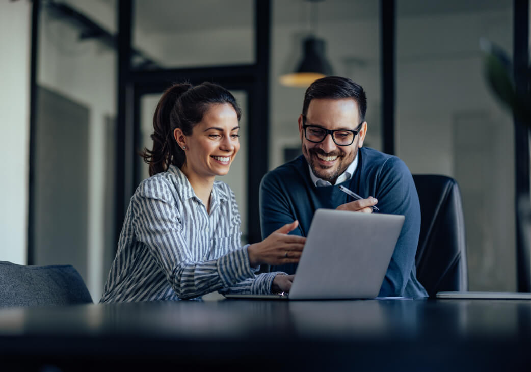 two people looking at a laptop and smiling while one of them points at the screen