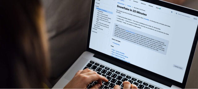 A data engineer works on a laptop while looking at Snowflake documentation