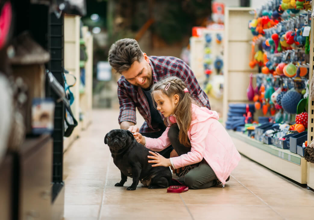 An adult and a child sitting on the floor of a pet store, petting their dog