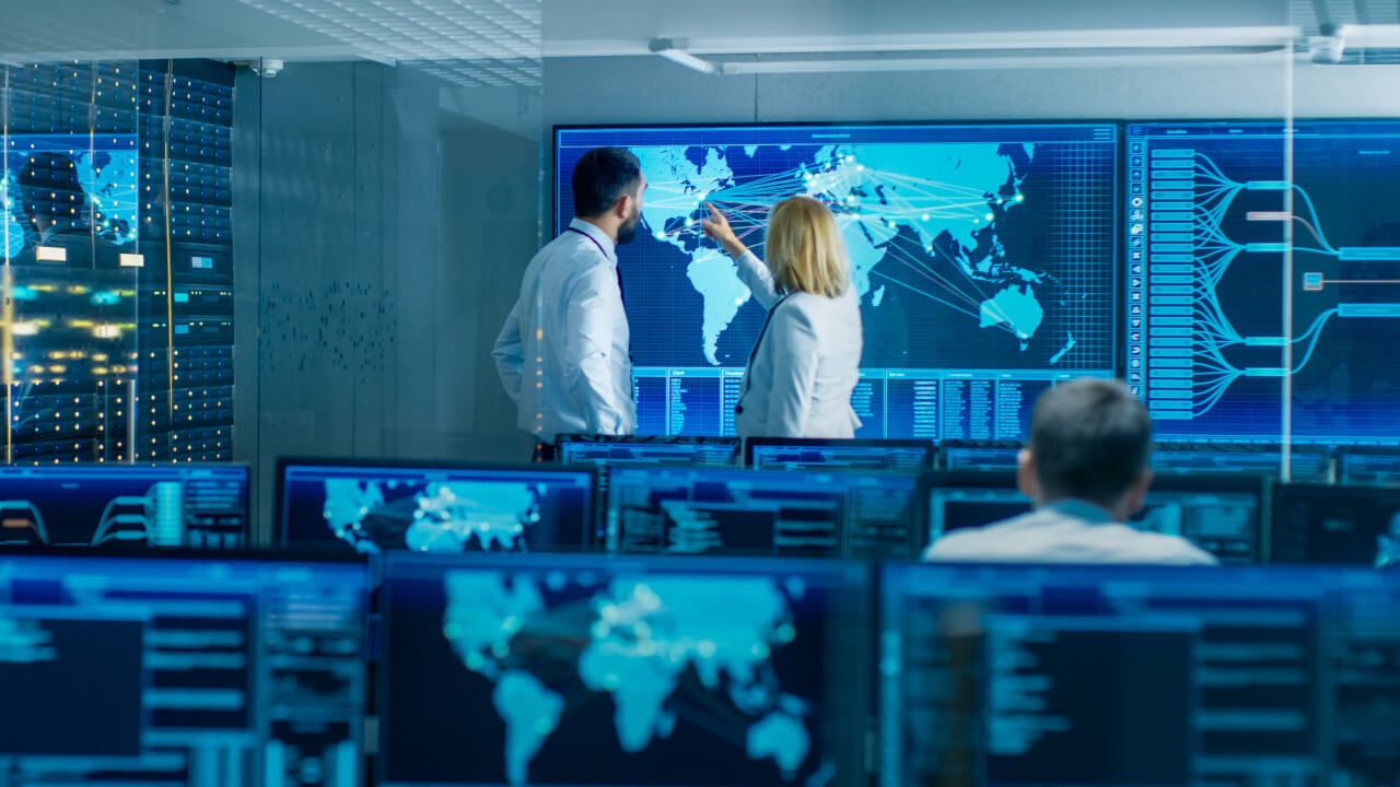 Employees looking at a series of network connections on a map of the world on a screen